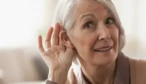 An older woman is touching her ear with her hand trying to hear